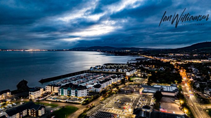 View of a coastal town at dusk, with lights reflecting on the water.