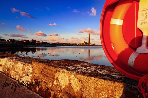 Lifebuoy on a wall with a scenic river view and a tower in the background at sunset.