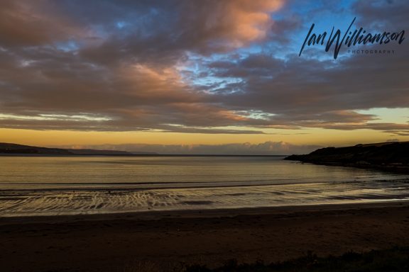 Serene beach at sunset with calm waters and colourful sky.