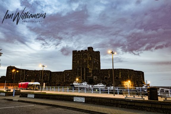 Historic castle with dramatic clouds and foreground lights at dusk.