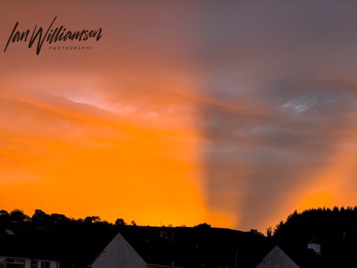 Dramatic sunset with orange hues and dark silhouettes of hills and clouds.
