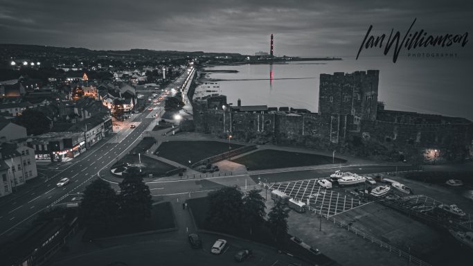 Coastal town at dusk, featuring buildings, a park, and a calm sea.