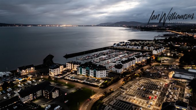 Aerial view of a coastal town at dusk, featuring lights reflecting on the water.