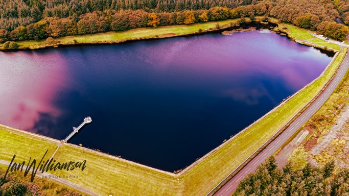 Aerial view of a large, tranquil lake surrounded by greenery and a pathway.