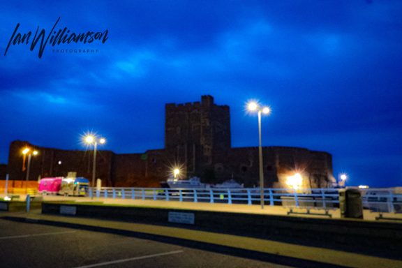 A castle silhouette against a blue evening sky with streetlights illuminating the area.