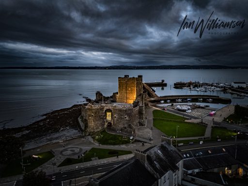 Ruins of a castle by the water under a dramatic stormy sky.
